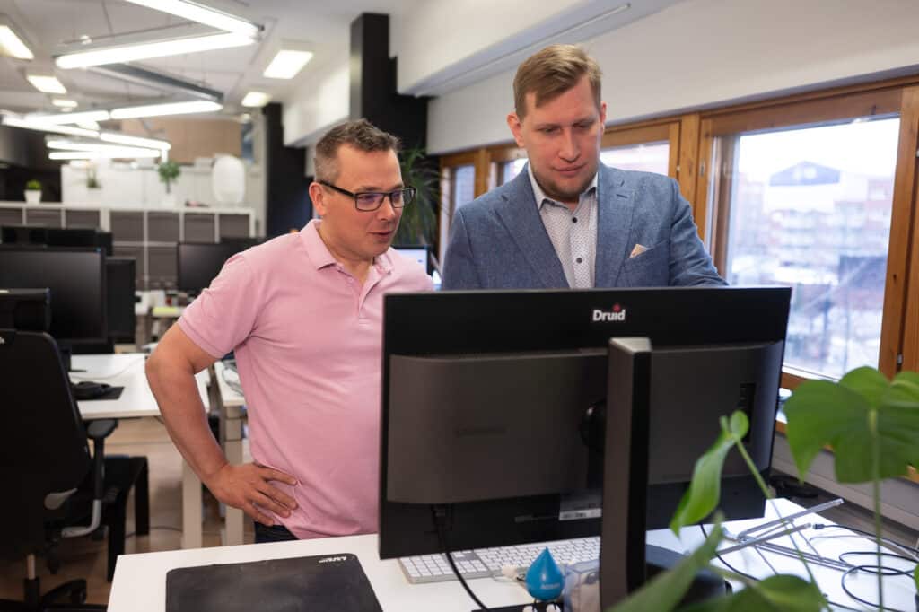 Kaksi miestä keskustelee tietokoneen äärellä.
