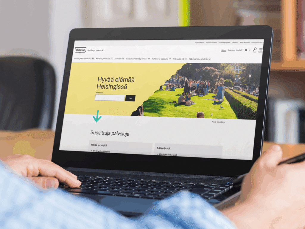 Hel.fi:n etusivu kannettavan tietokoneen näytöllä. Miehen vasen käsi näppäimistöllä ja toinen käsi lepää tietokoneen vieressä.
