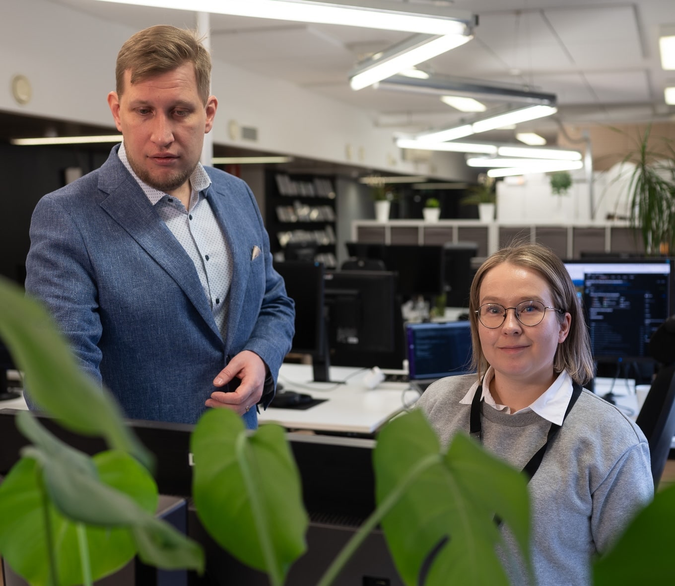Mies katsoo näyttöön ja nainen suoraan kohti toimistoympäristössä.